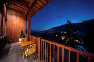 Un balcón de madera con una mesa y sillas, con vistas a un paisaje nevado al anochecer.