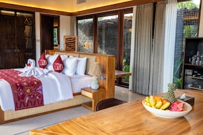 A hotel room with a bed, bedside table, lamp, and a bowl of fruit on a wooden table. - Kropak Sidemen (Sidemen)