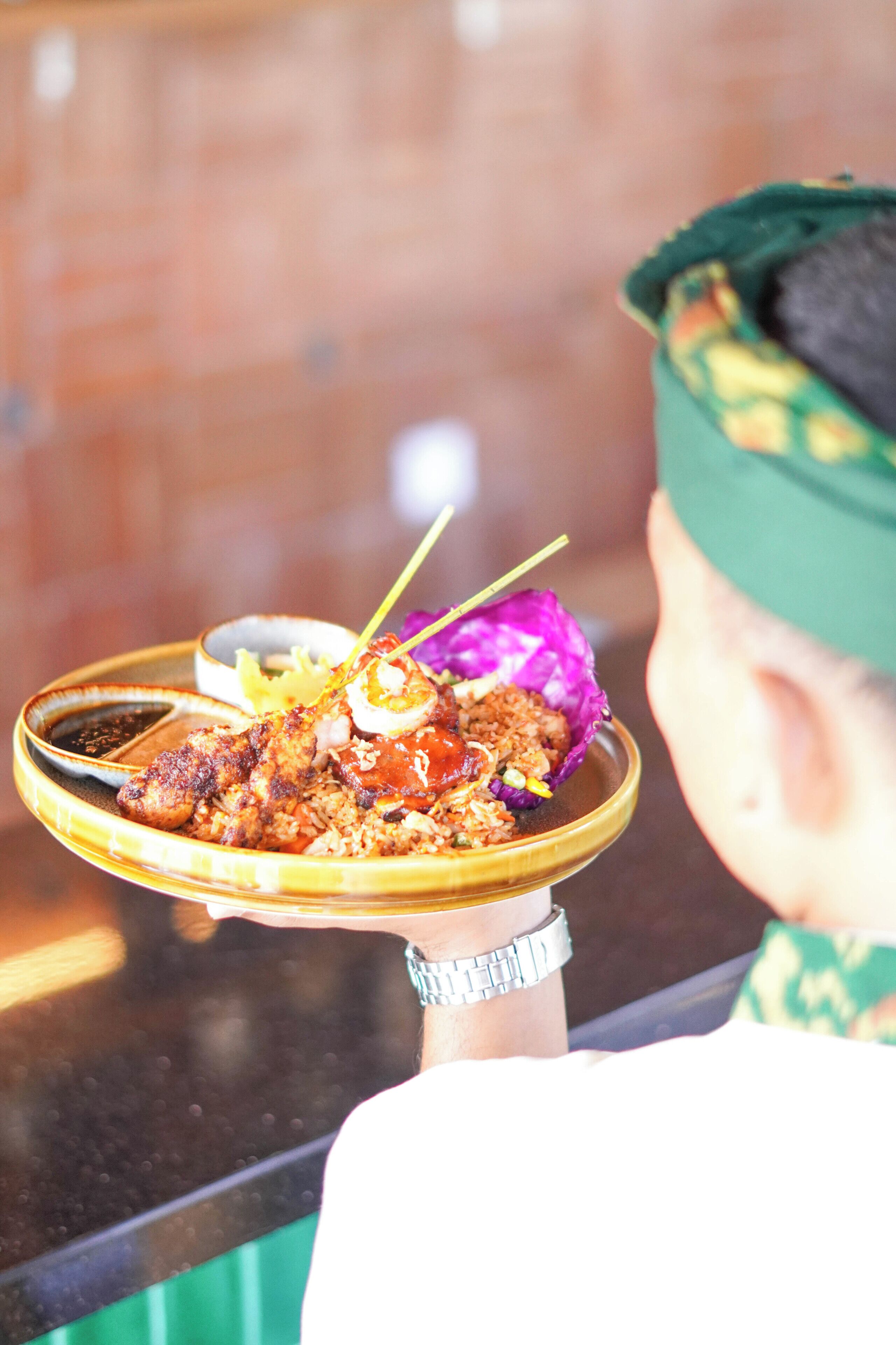 A person holding a tray with food, wearing a green cap and a watch.