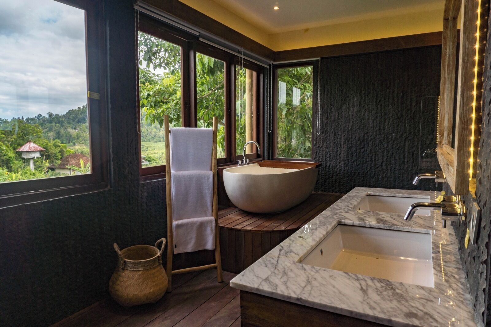 A modern bathroom with a large freestanding bathtub, a marble sink, and a view of greenery outside.
