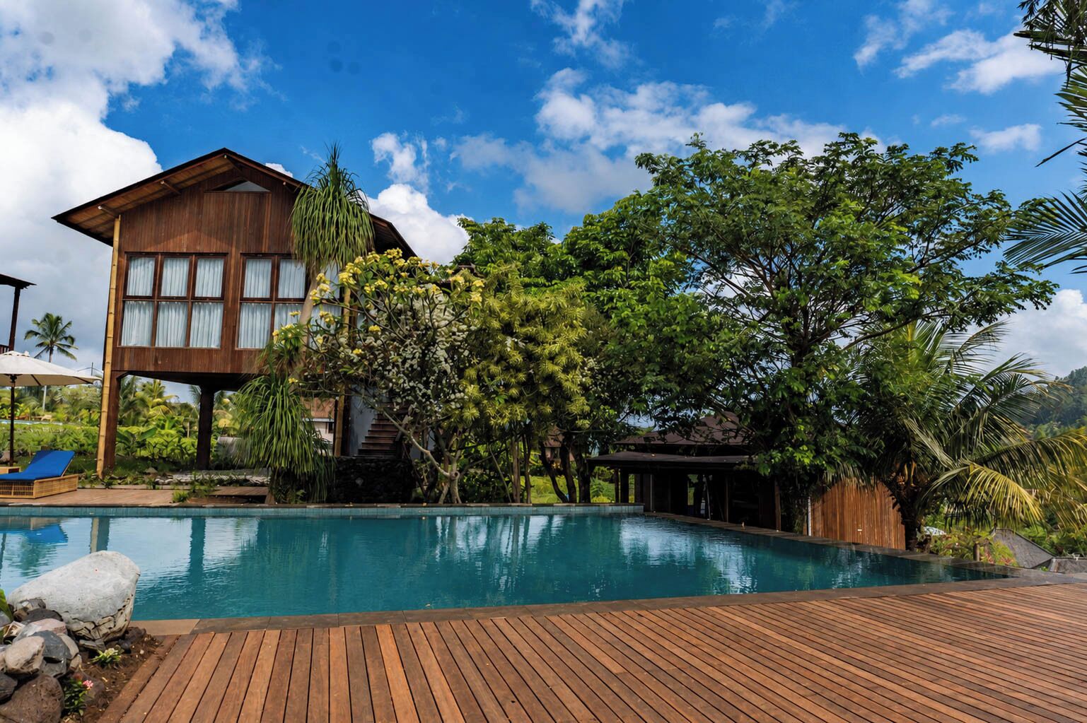 A wooden deck leading to a clear blue pool with a large building in the background.
