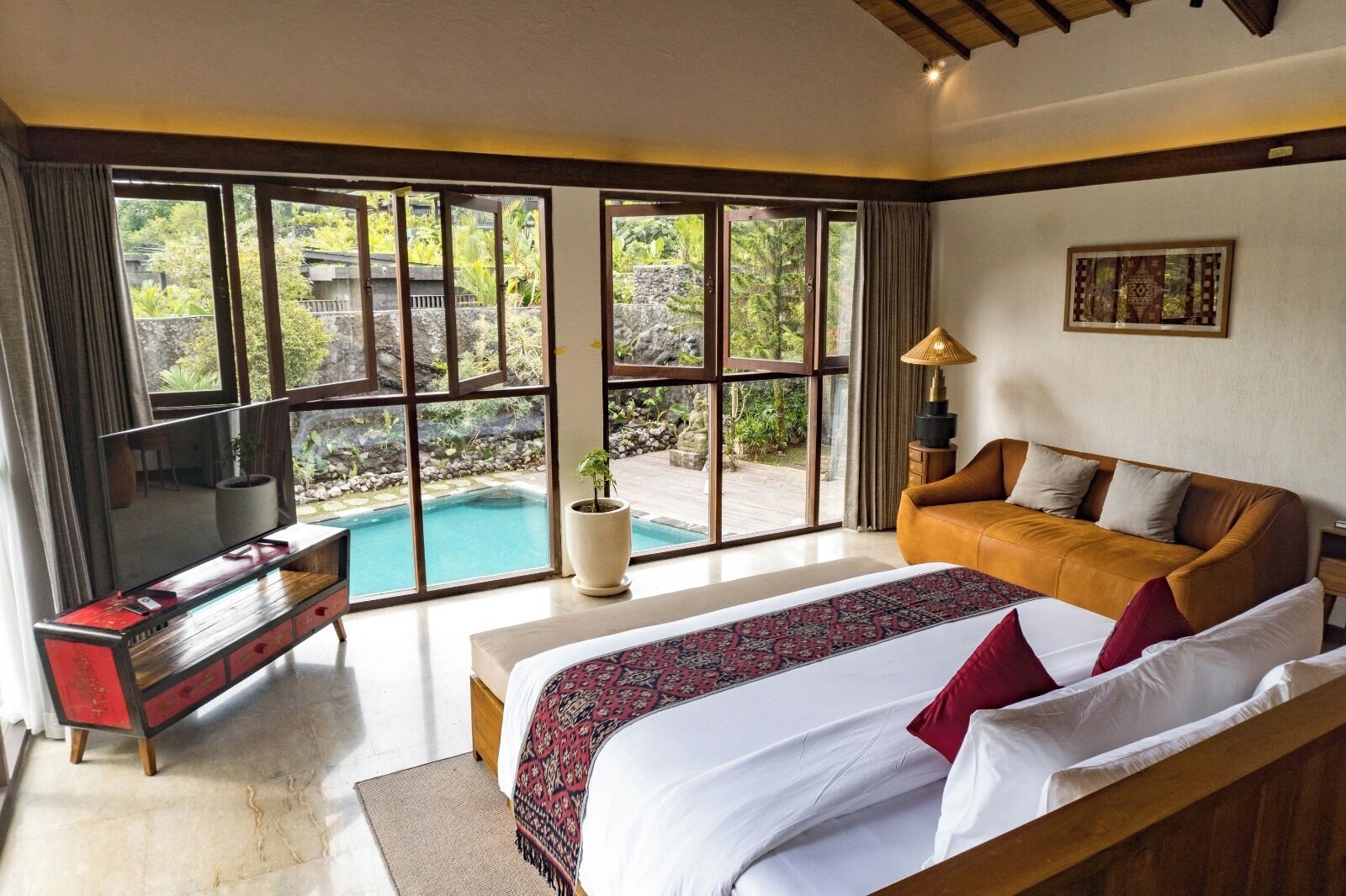 A bedroom with a large bed, a sofa, a TV, and a view of a swimming pool.