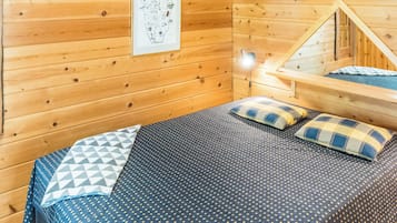 Una stanza in legno con un letto, cuscini, una mappa appesa al muro e un tavolino.