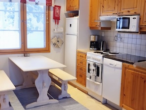 Una cocina compacta con armarios de madera, encimera blanca, microondas, cafetera y lavavajillas.
