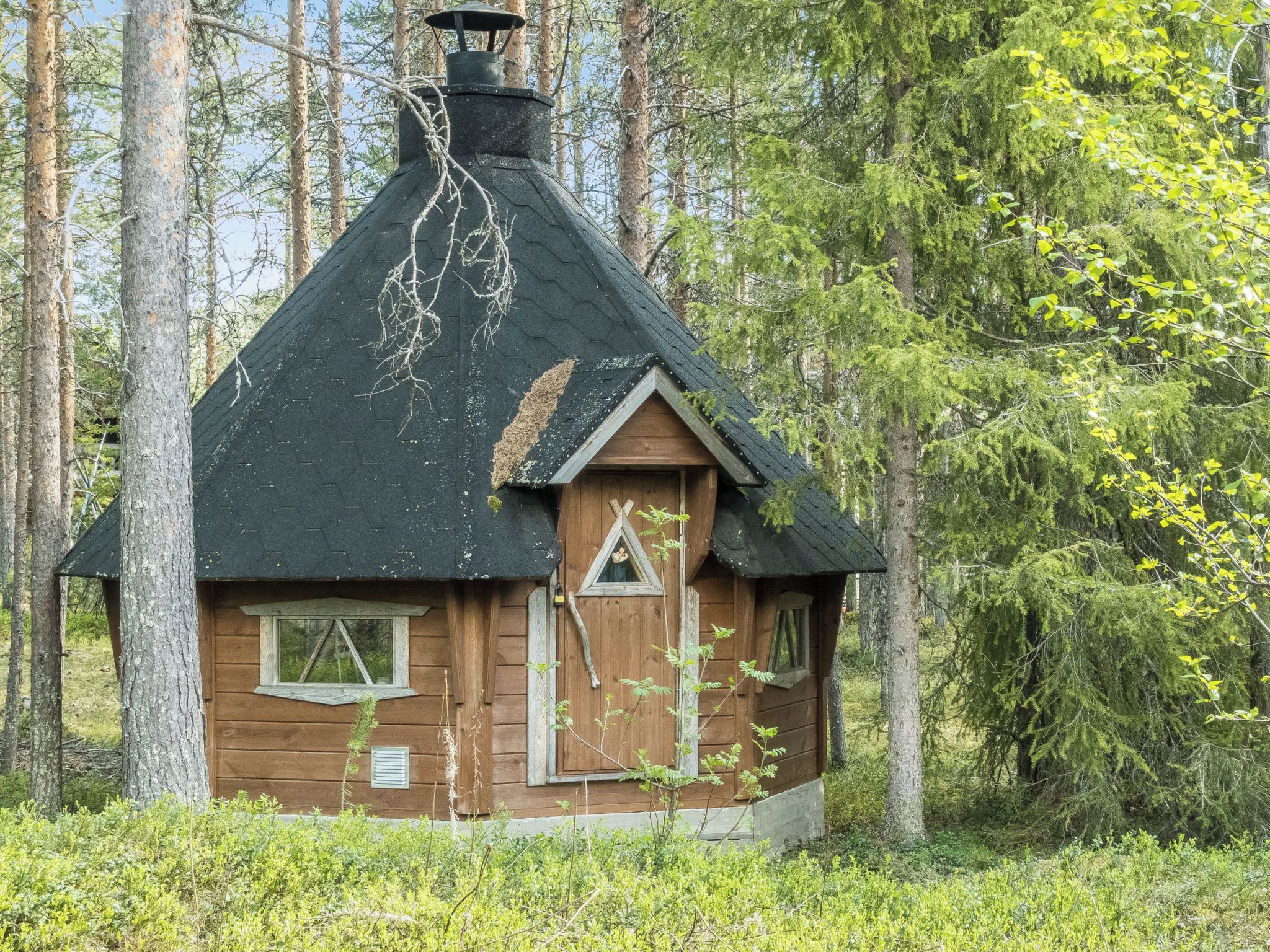 Una pequeña cabaña de madera con techo pronunciado, una chimenea y un ventanal triangular.