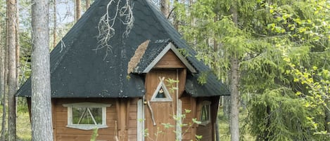 A small wooden cabin with a steeply pitched roof, a chimney, and a small triangular window.