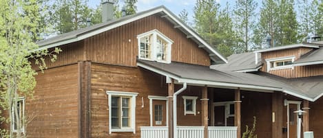 Een houten woonhuis met twee verdiepingen, een veranda, schoorsteen en een kleine aangebouwde garage.