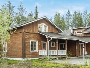 Une maison en bois à deux étages, dotée d’un porche, d’une cheminée et d’un petit garage attenant.