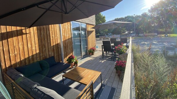 Una terraza de madera con un sofá, una mesa y una sombrilla que da sombra.