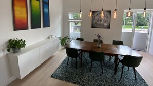 Un comedor moderno con una mesa de madera, sillas negras, un tapete oscuro y lámparas colgantes.