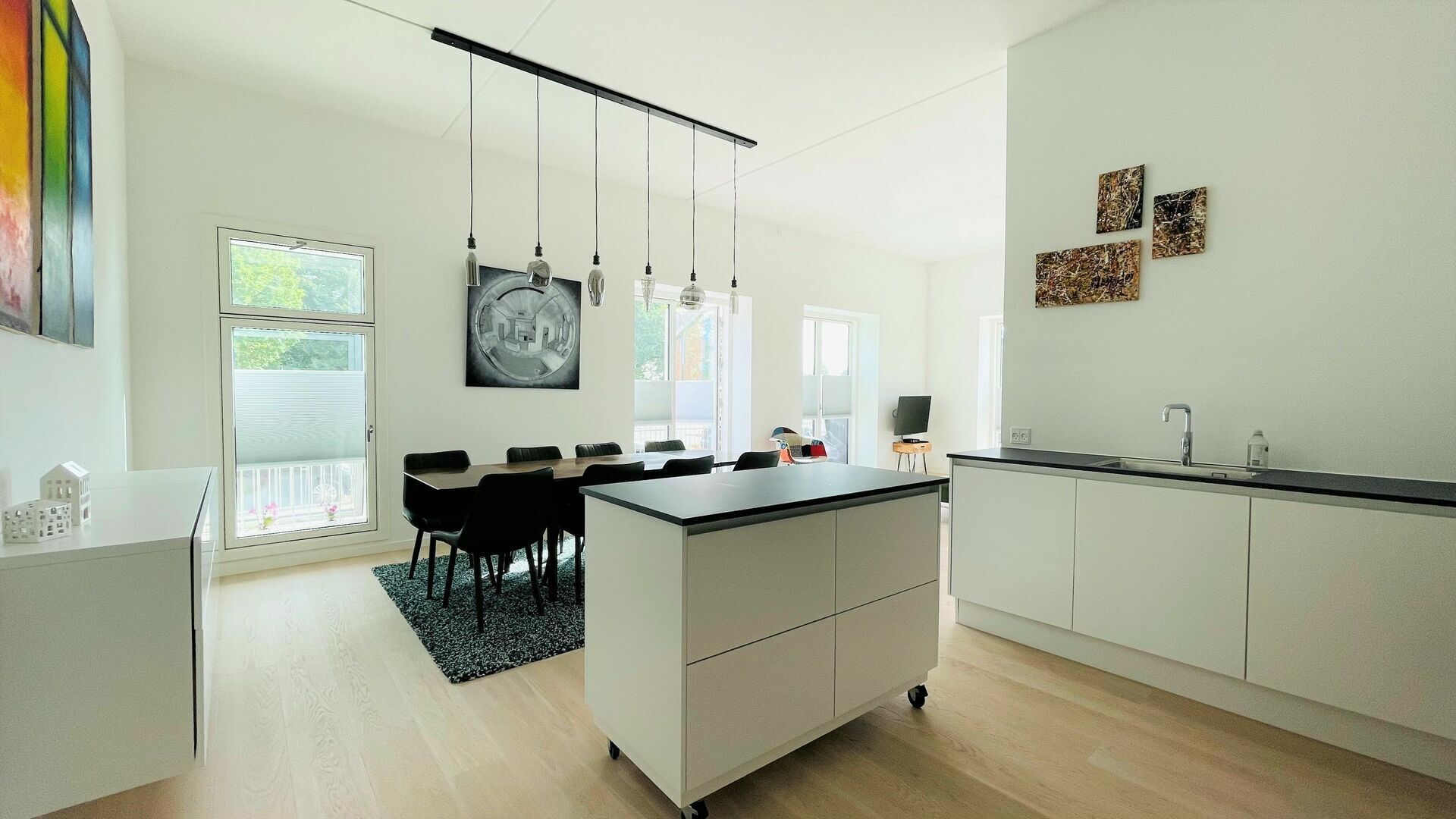 Une cuisine moderne dotée d’un îlot central, de meubles blancs et de luminaires suspendus.