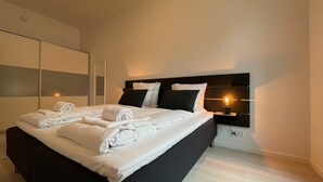 Una habitación de hotel moderna con una cama grande, cabecera negra, ropa de cama blanca y una mesita de noche con lámpara.