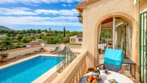 A balcony with a pool, a table with fruits and a cup, and a view of a green landscape. - Isabelle by Interhome (Jávea)