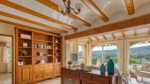 A spacious living room with wooden furniture, a large window with a view of the countryside, and a ceiling with exposed beams. - Isabelle by Interhome (Jávea)