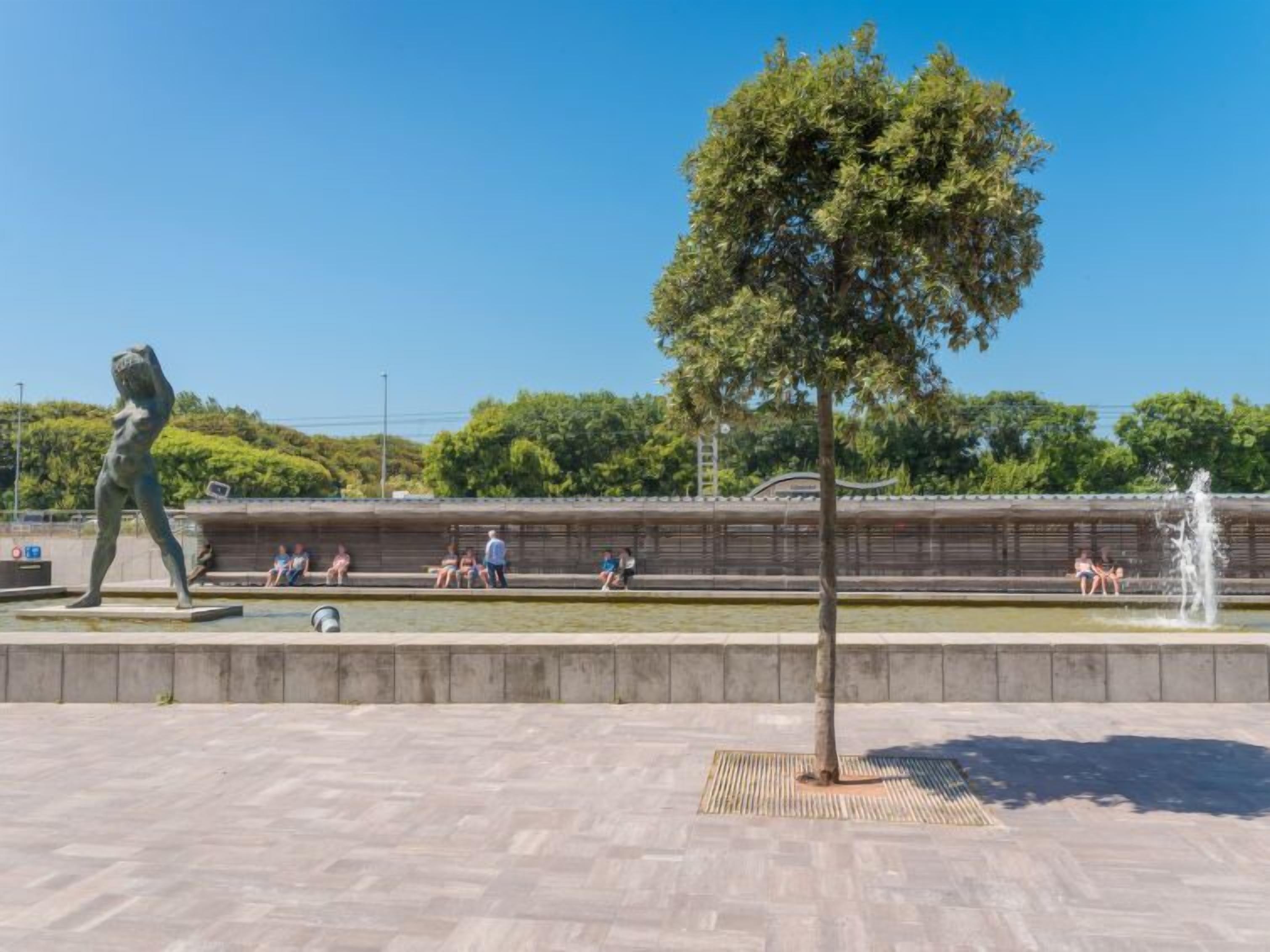En offentlig plads med en statue, en springvand og et træ.