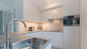 Cozinha moderna com pia de aço inoxidável, armários brancos e forno embutido.