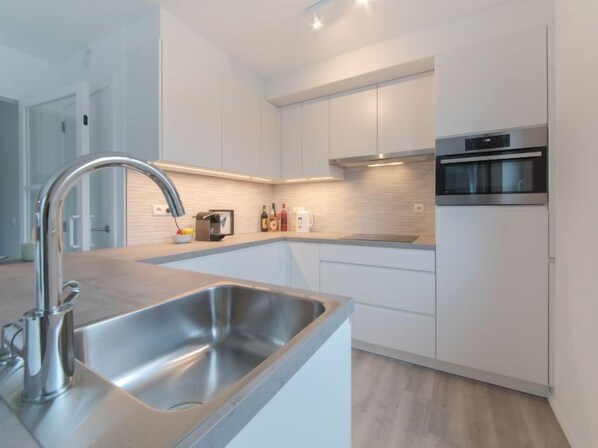 A modern kitchen with a stainless steel sink, white cabinets, and a built-in oven. - Medano with balcony by Interhome (Bredene)