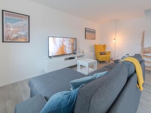 A modern living room with a grey sofa, a yellow armchair, a flat-screen TV, and a staircase in the background.