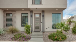 A modern two-story building with a gray facade, a front door with a glass panel, and a small porch area with steps leading to the entrance. - Red Desert Loft Resort 37| Pickleball Courts, Foosball, Resort Pool with Waterslide & Jacuzzi! (Saint George)
