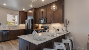 A modern kitchen with dark wooden cabinets, stainless steel appliances, and a central island with bar stools. - Red Desert Loft Resort 37| Pickleball Courts, Foosball, Resort Pool with Waterslide & Jacuzzi! (Saint George)