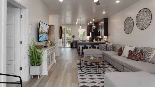 A modern living room with a sofa, coffee table, and a TV. There is a kitchen area with a bar and stools. - Red Desert Loft Resort 37| Pickleball Courts, Foosball, Resort Pool with Waterslide & Jacuzzi! (Saint George)