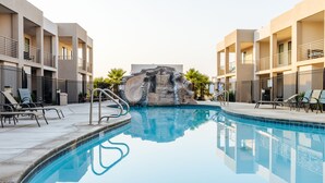 A swimming pool with a waterfall feature, surrounded by lounge chairs and a modern building facade. - Red Desert Loft Resort 37| Pickleball Courts, Foosball, Resort Pool with Waterslide & Jacuzzi! (Saint George)