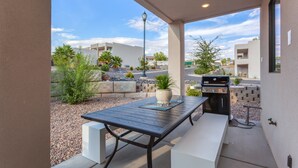 An outdoor patio with a table and grill, surrounded by a landscaped garden and residential buildings in the background. - Red Desert Loft Resort 37| Pickleball Courts, Foosball, Resort Pool with Waterslide & Jacuzzi! (Saint George)