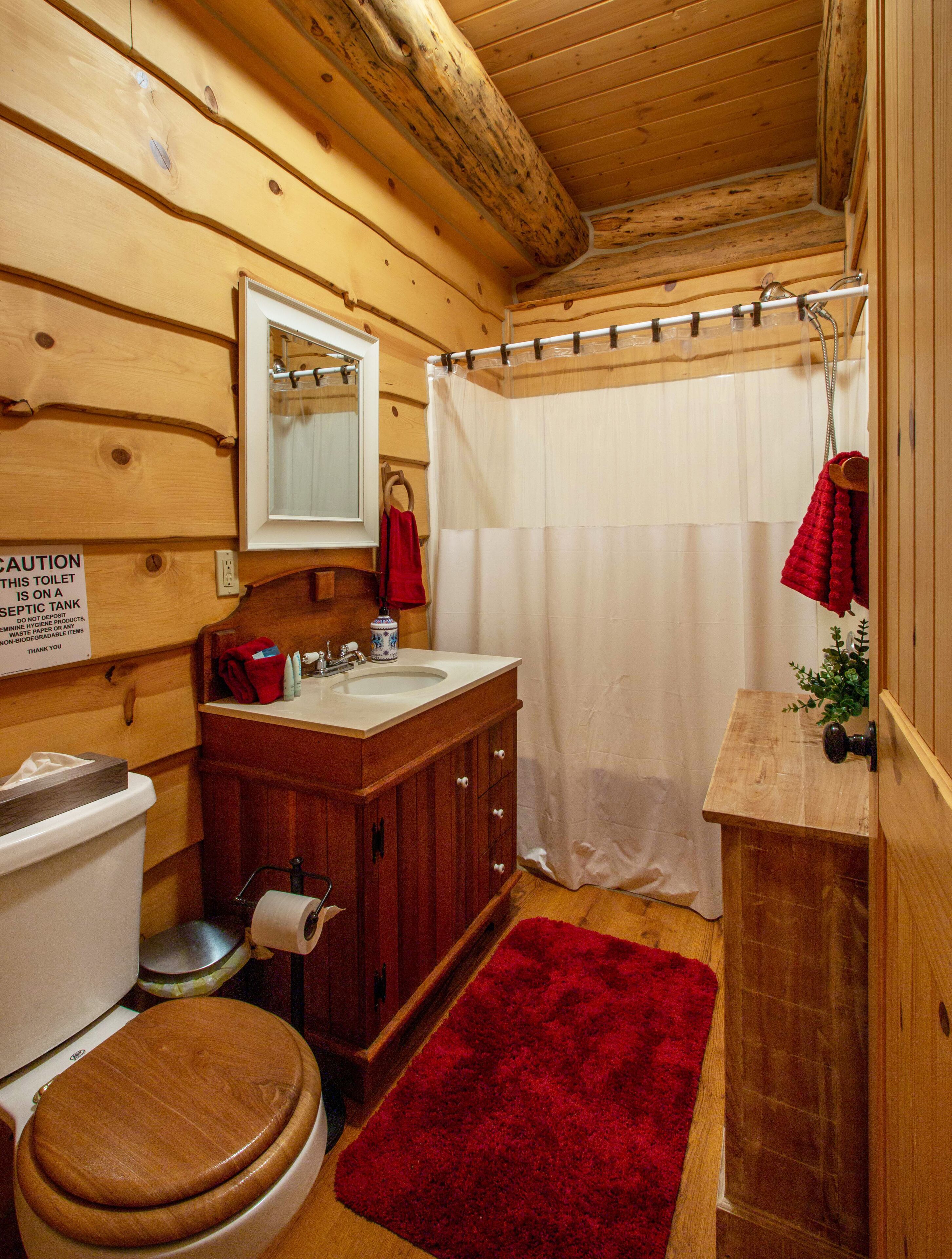 A wooden cabin bathroom with a toilet, sink, and shower curtain.