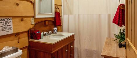 A wooden cabin bathroom with a toilet, sink, and shower curtain.