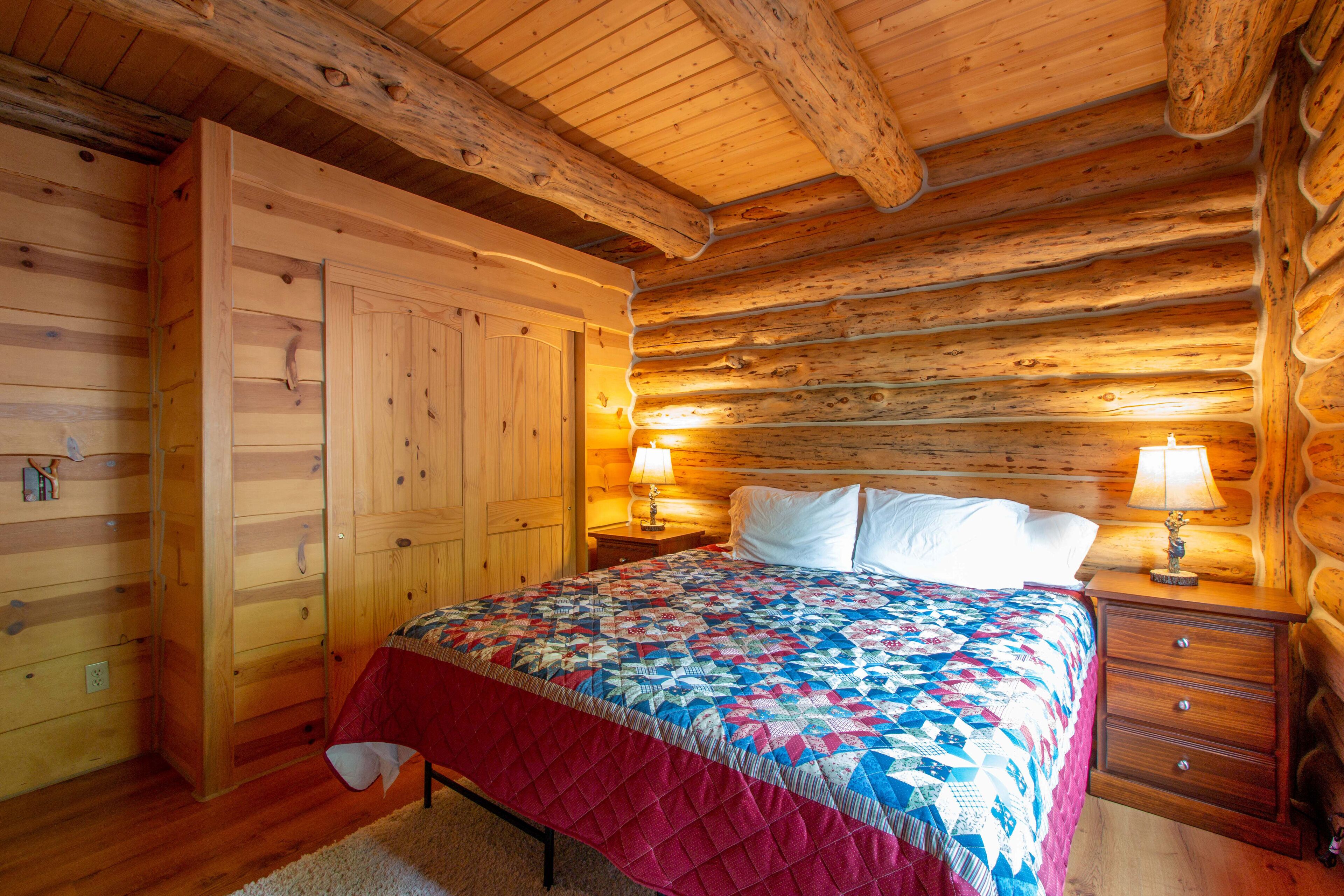 Un dormitori de cabana de fusta amb un llit de fusta, una tauleta de nit amb una làmpada i un armari de fusta.