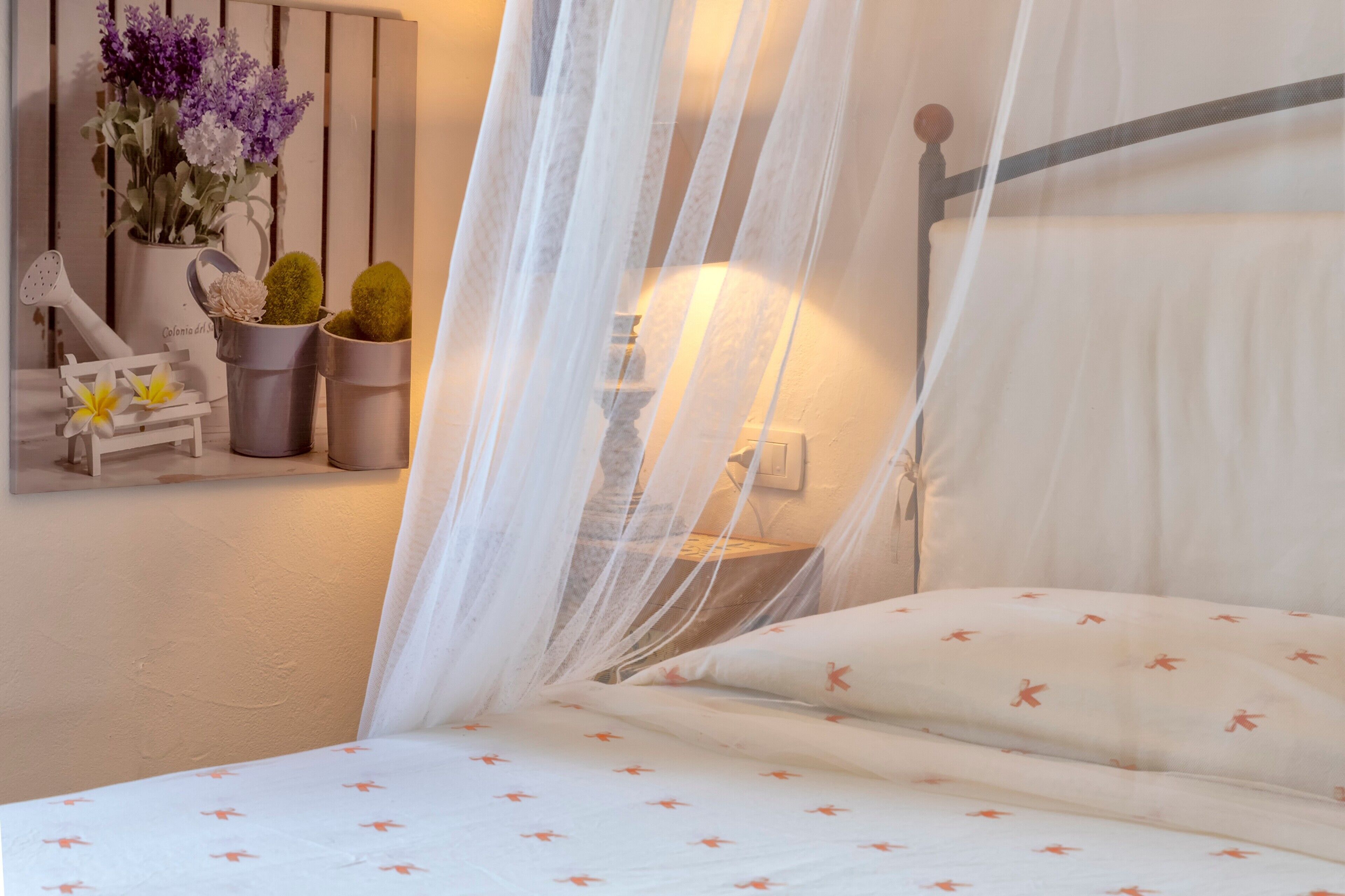 Ein Bett mit Baldachin, ein Nachttisch mit Lampe sowie ein an der Wand befestigtes Regal mit Dekoration.