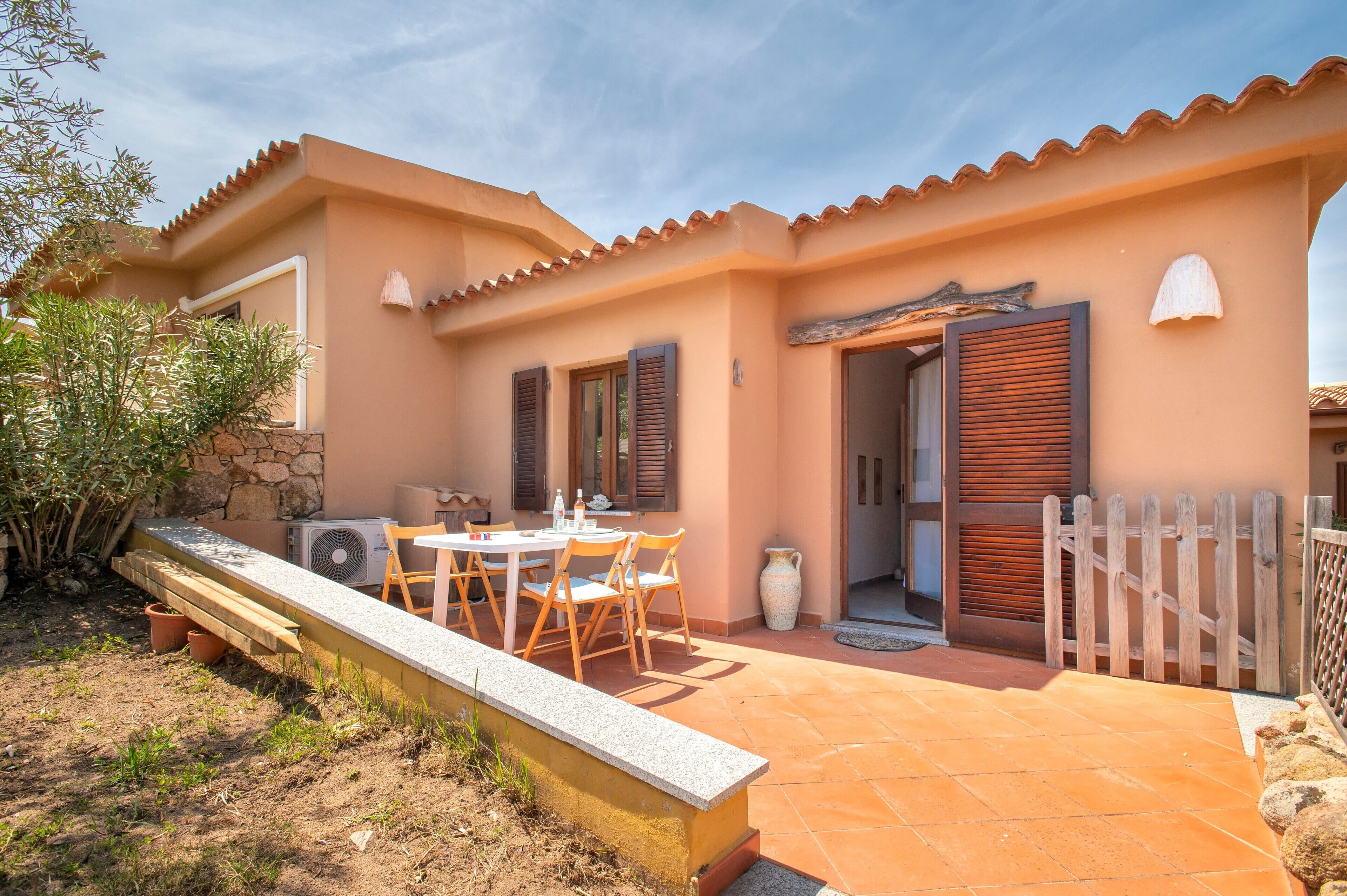 Una casa con un patio, una mesa con sillas, un muro de piedra y una valla de madera.