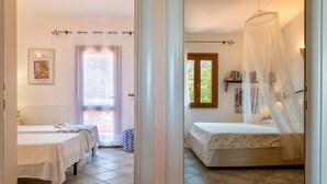 Quarto com duas camas, janela com cortinas, mesa de cabeceira e estante de livros.