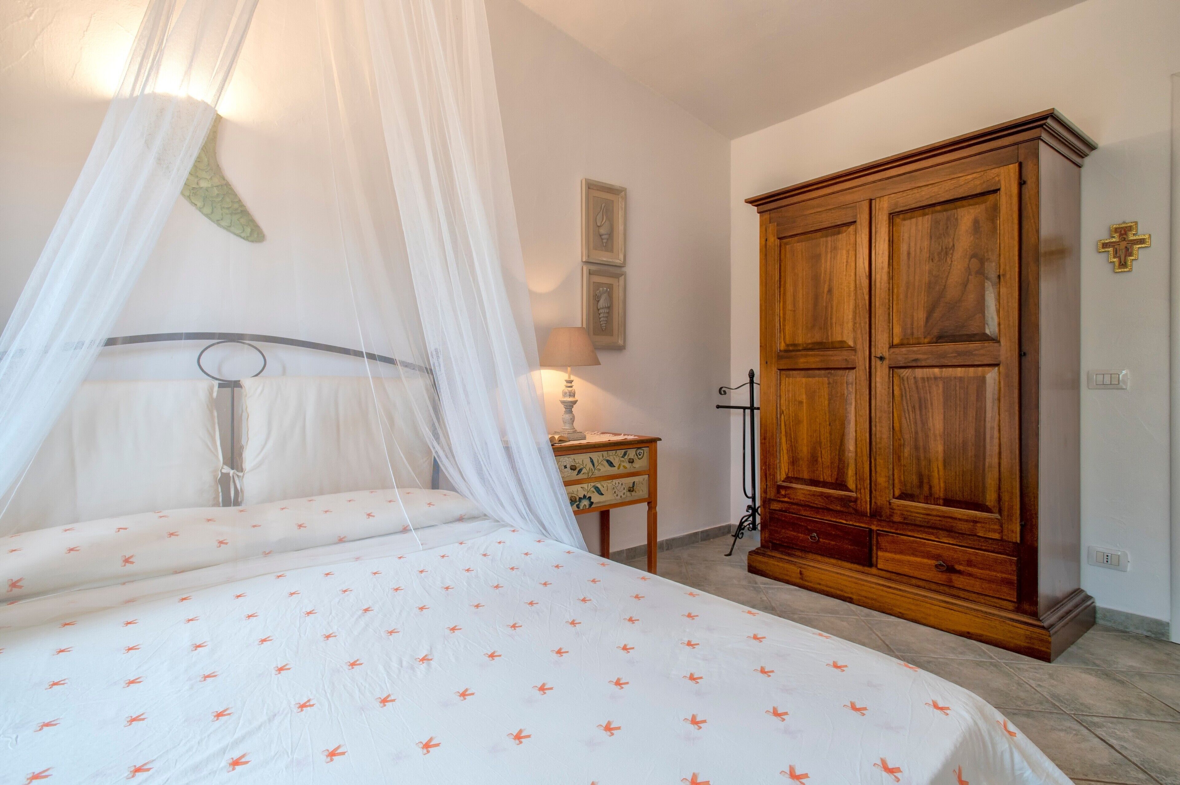 Un dormitorio con una cama, un armario de madera, una mesita de noche y una lámpara de pared.