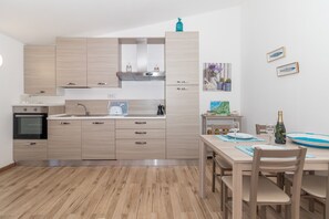A modern kitchen with light wood cabinetry, a built-in oven, and a dining area with a wooden table and chairs.