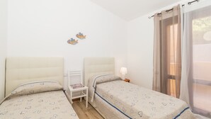 Un dormitorio con dos camas, una mesita de noche, una lámpara y una ventana con cortinas.