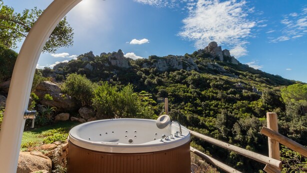 Un jacuzzi con cubierta de madera, rodeado por una valla de madera, con vistas a un paisaje montañoso de riscos y vegetación.