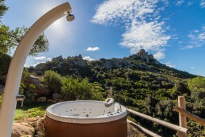Un jacuzzi con cubierta de madera, rodeado por una valla de madera, con vistas a un paisaje montañoso de riscos y vegetación.