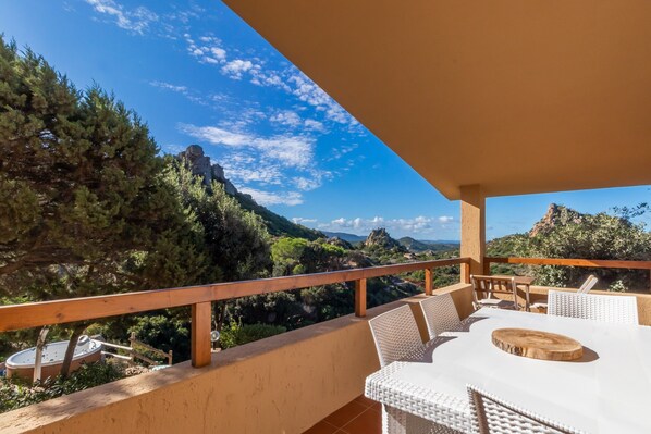 A balcony with a table and chairs, overlooking a mountainous landscape.