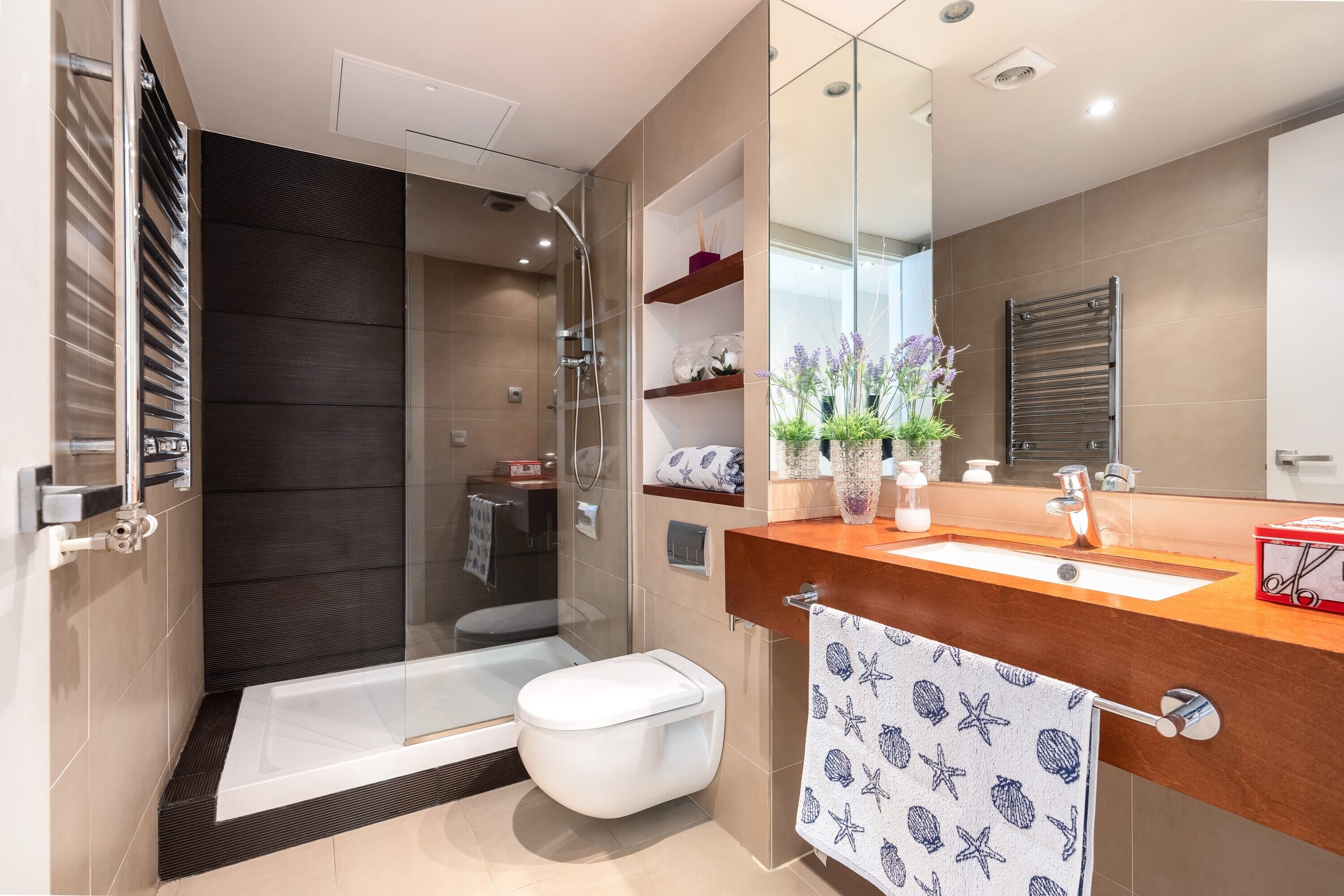 Un baño moderno con cabina de ducha de vidrio, bañera, inodoro, tocador con espejo y un perchero para toallas.
