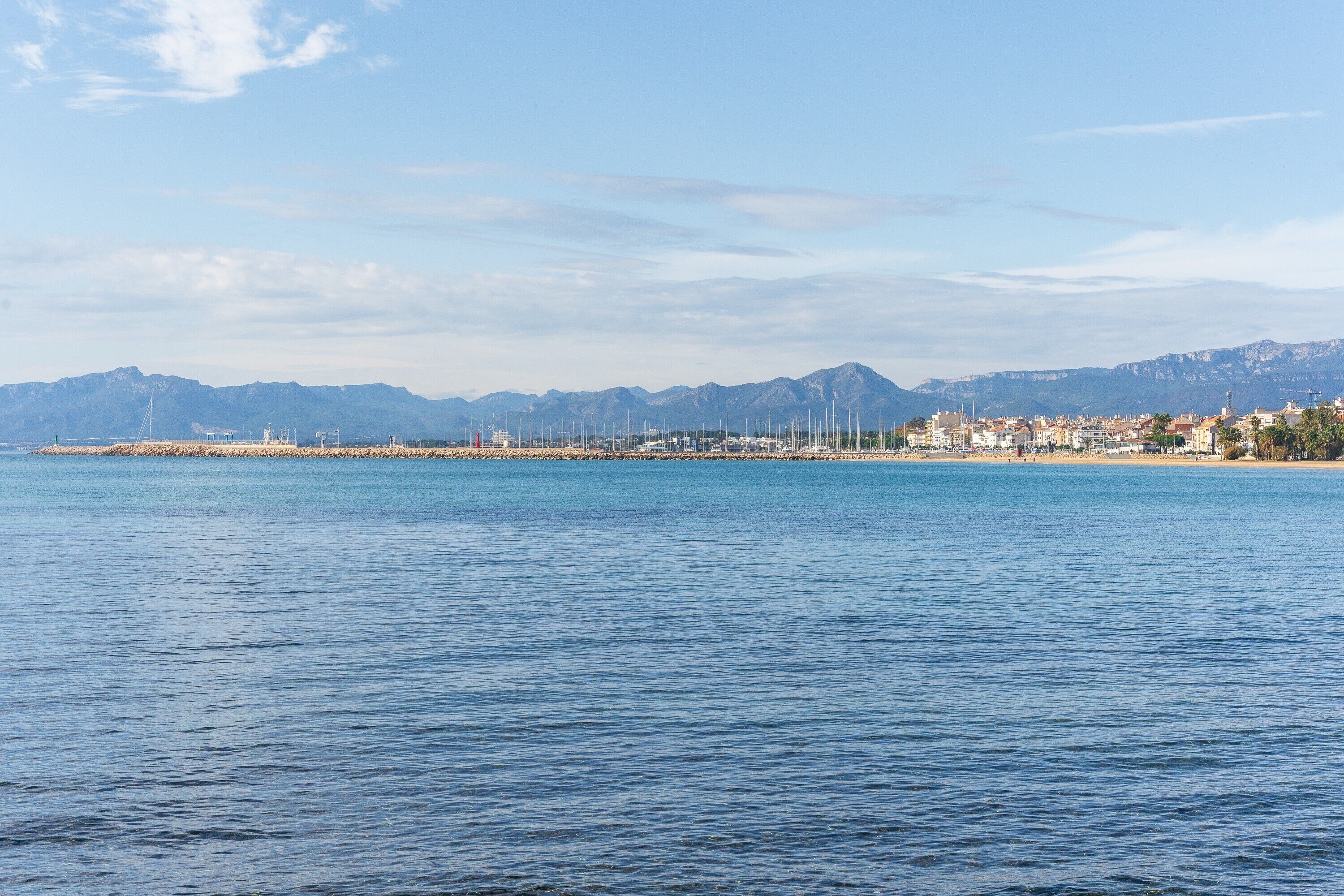 Un paysage urbain côtier avec un port de plaisance, des bâtiments et des montagnes en arrière-plan.