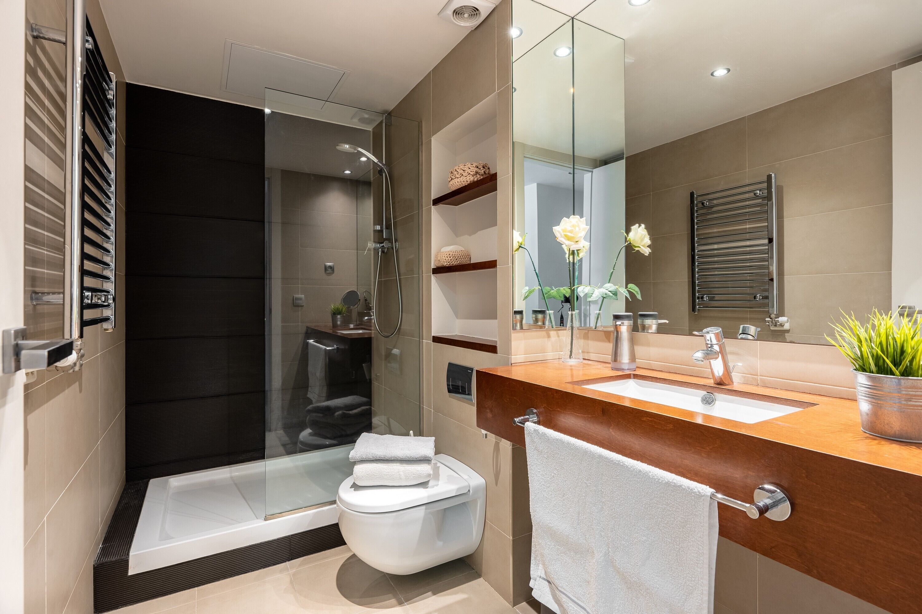 A modern bathroom with a glass shower enclosure, a white toilet, a wooden vanity with a sink, and a mirror.