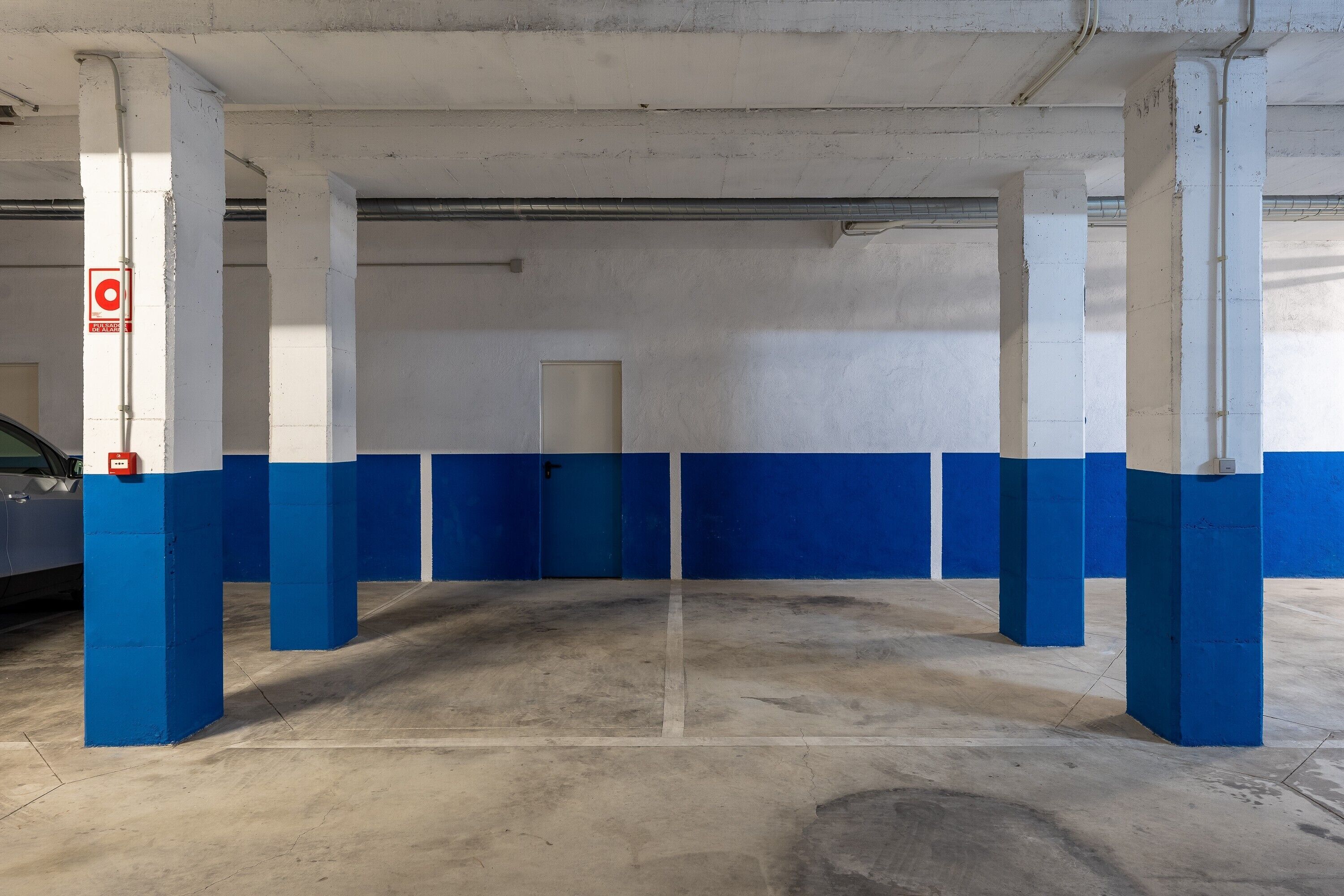 Een parkeergarage met blauwe en witte pilaren, een betonnen vloer en een deur op de achtergrond.