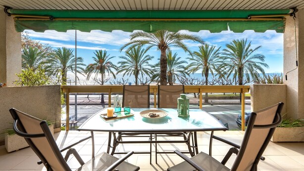 Un espacio de estar techado al aire libre con una mesa, sillas y vistas a palmeras y al mar.