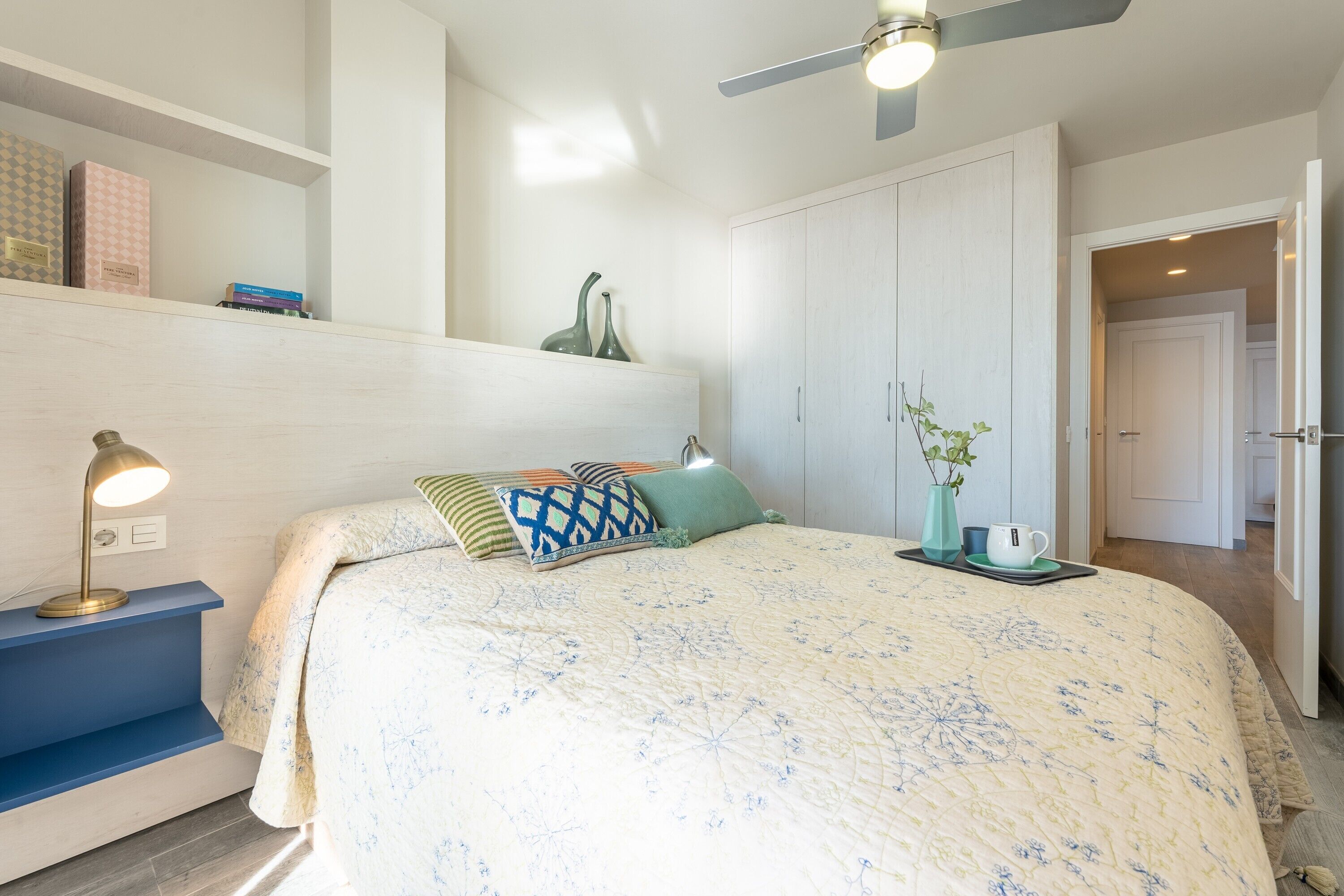 Une chambre à coucher avec un lit, une table de chevet, une lampe et un ventilateur de plafond.