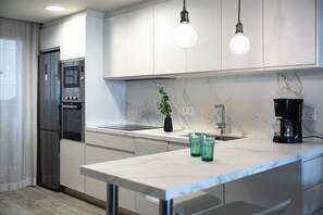 A modern kitchen with a built-in oven, a sink, a coffee maker, and pendant lighting. - Beachfront Apartment (Cambrils)