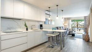 Una cocina moderna con gabinetes blancos, encimera de mármol y un comedor con mesa blanca y taburetes de bar.