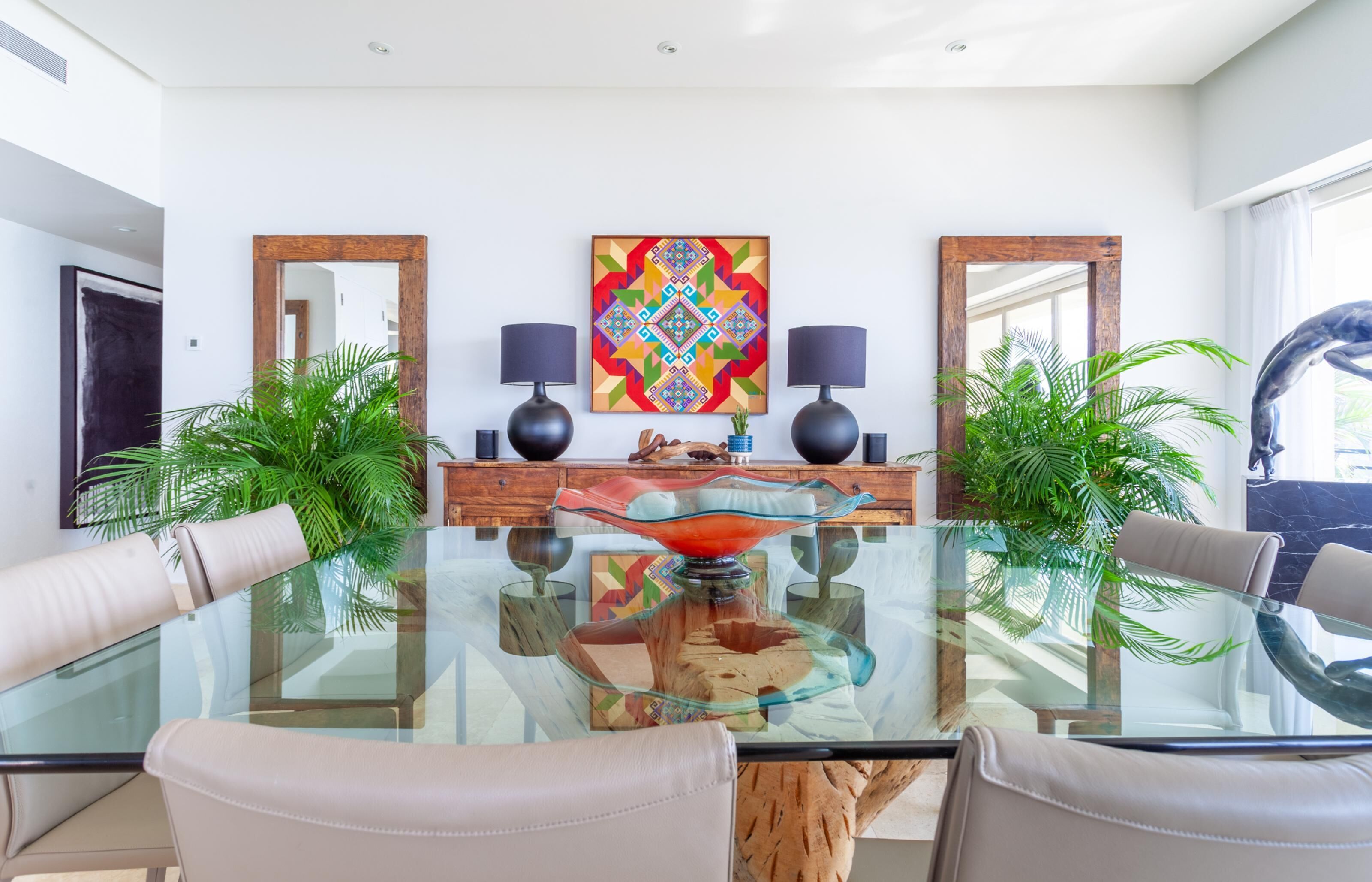 A modern dining area with a glass table, leather chairs, and a central decorative piece.