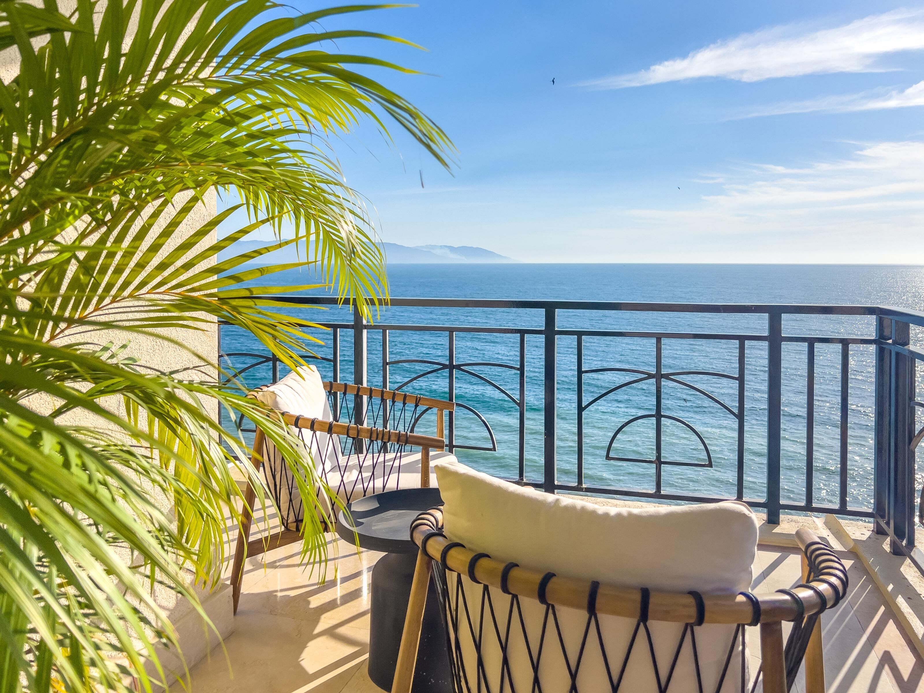 Un balcón con vista al mar, una silla y una palmera.
