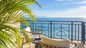 A balcony with a view of the sea, a chair, and a palm tree.